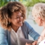 A caregiver smiles at an older client in a chair, representing the joy that can come from a healthy work-life balance.