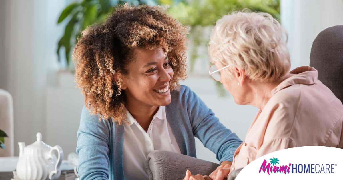 A caregiver smiles at an older client in a chair, representing the joy that can come from a healthy work-life balance.