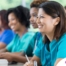 Several students in scrubs happily attend a class, representing caregiver training.