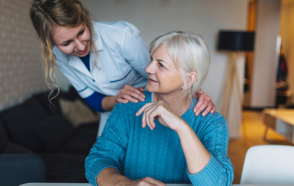 _Hollywood A smiling caregiver gently placing her hands on the shoulders of a senior woman in a cozy living room, representing compassionate home care in Hollywood.