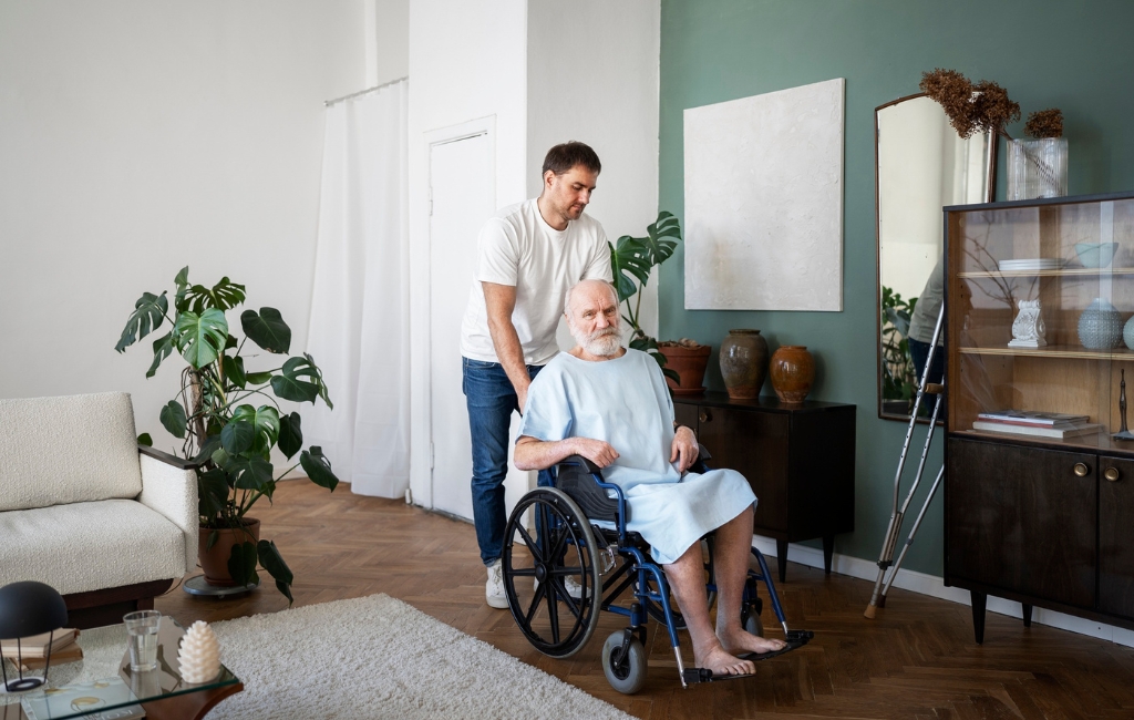 A caregiver provides home care in Sunrise, assisting an elderly man in a wheelchair inside a well-lit, cozy living room. The supportive environment reflects attentive and compassionate care.