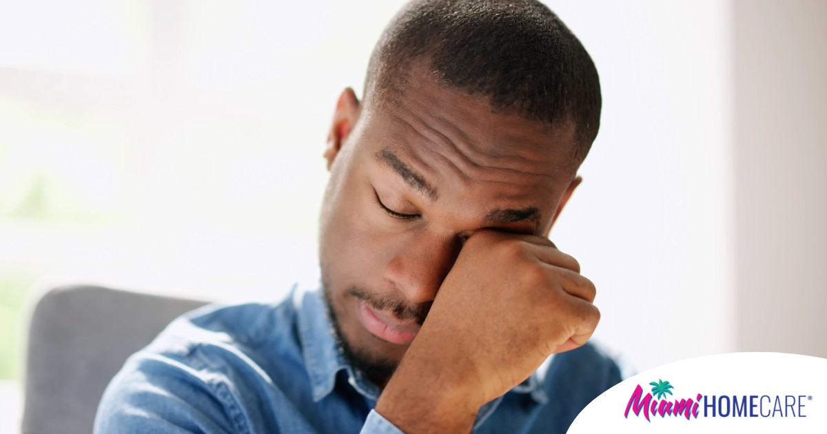 A man tiredly rubs his eyes, representing the exhaustion that can come with family caregiving.